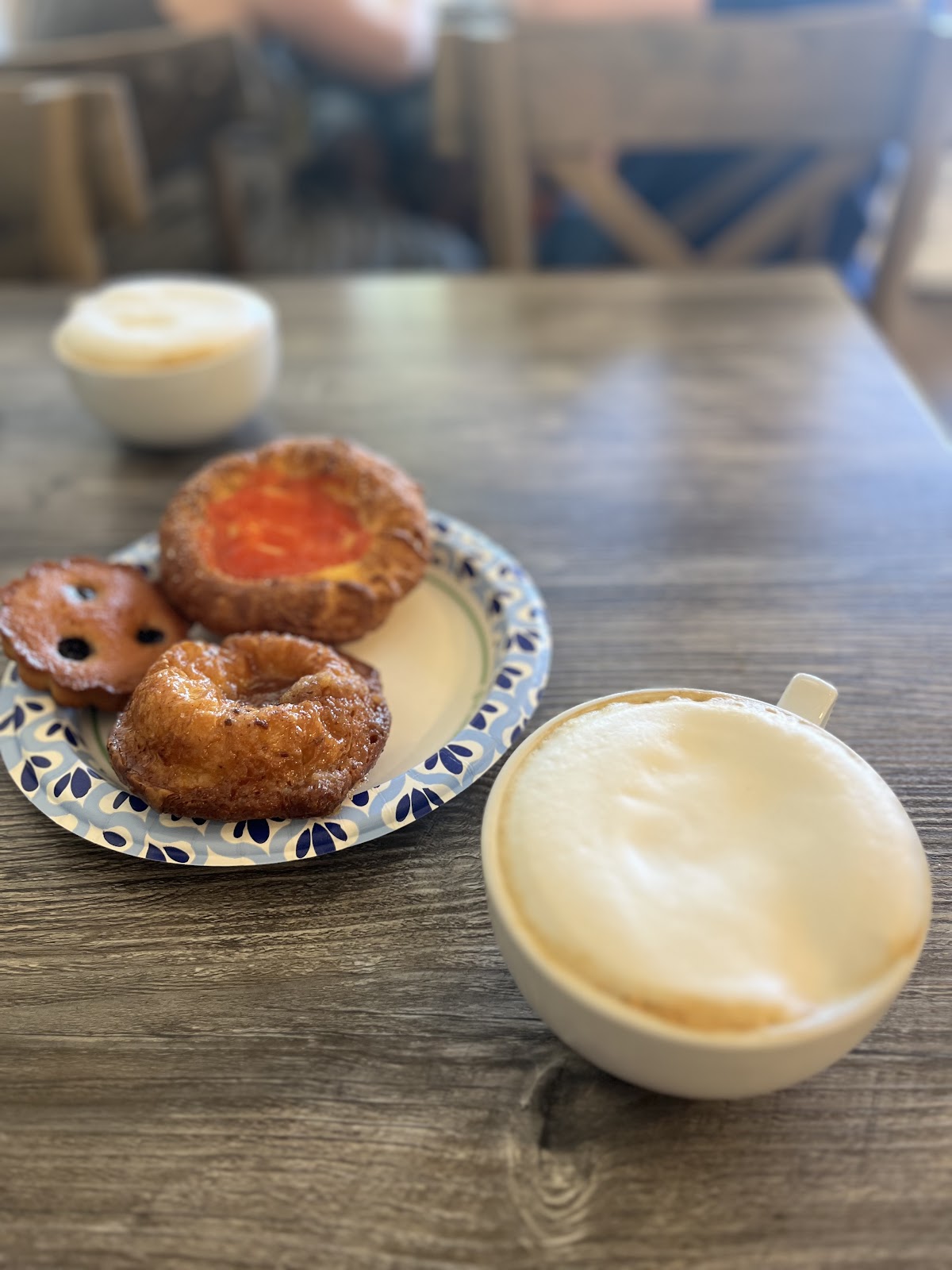 A cappuccino beside a kouign amann and a blueberry financier